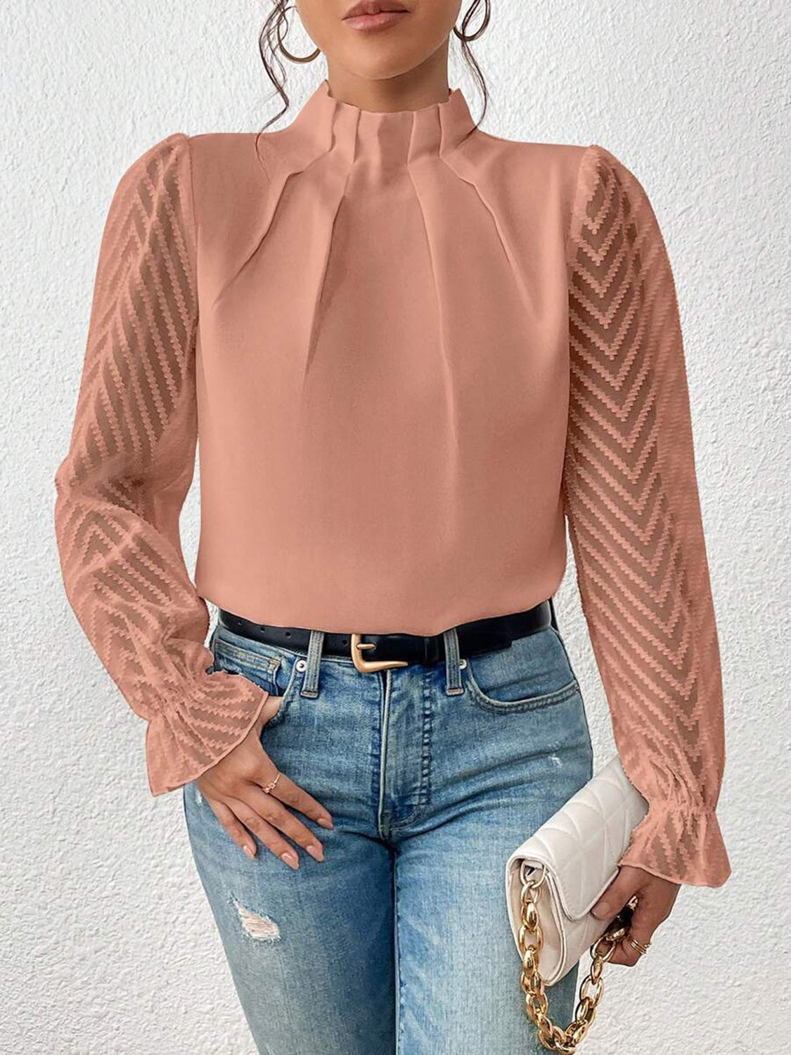 A stack of various coloured ruffled mock neck blouses, from cream to navy, neatly folded.