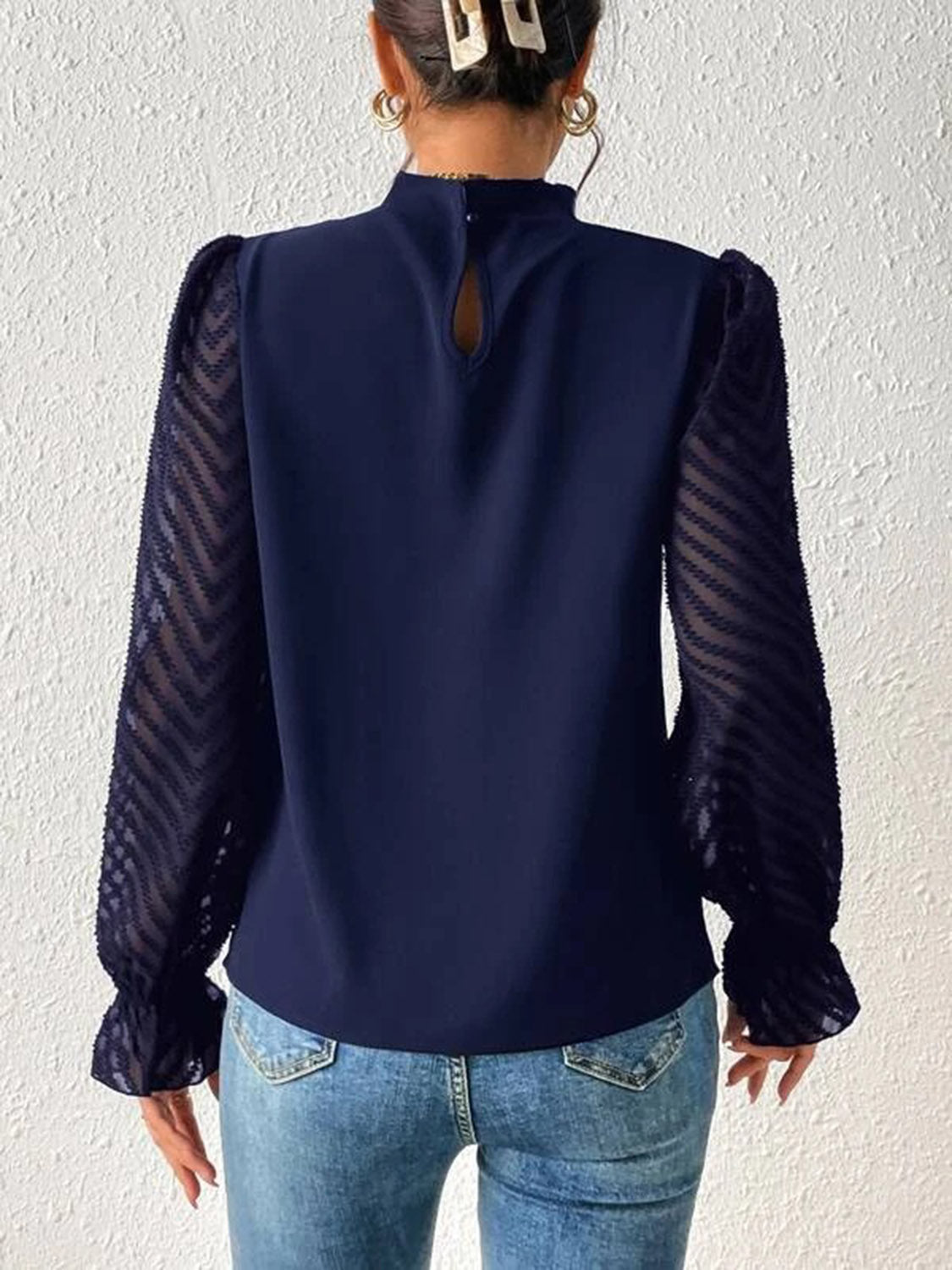 Side profile of the navy ruffled mock neck blouse, highlighting the flounce sleeves and semi-sheer texture.