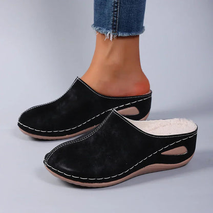 Model wearing brown Seraphina orthopaedic comfort slippers while standing on a wooden floor, full body shot.