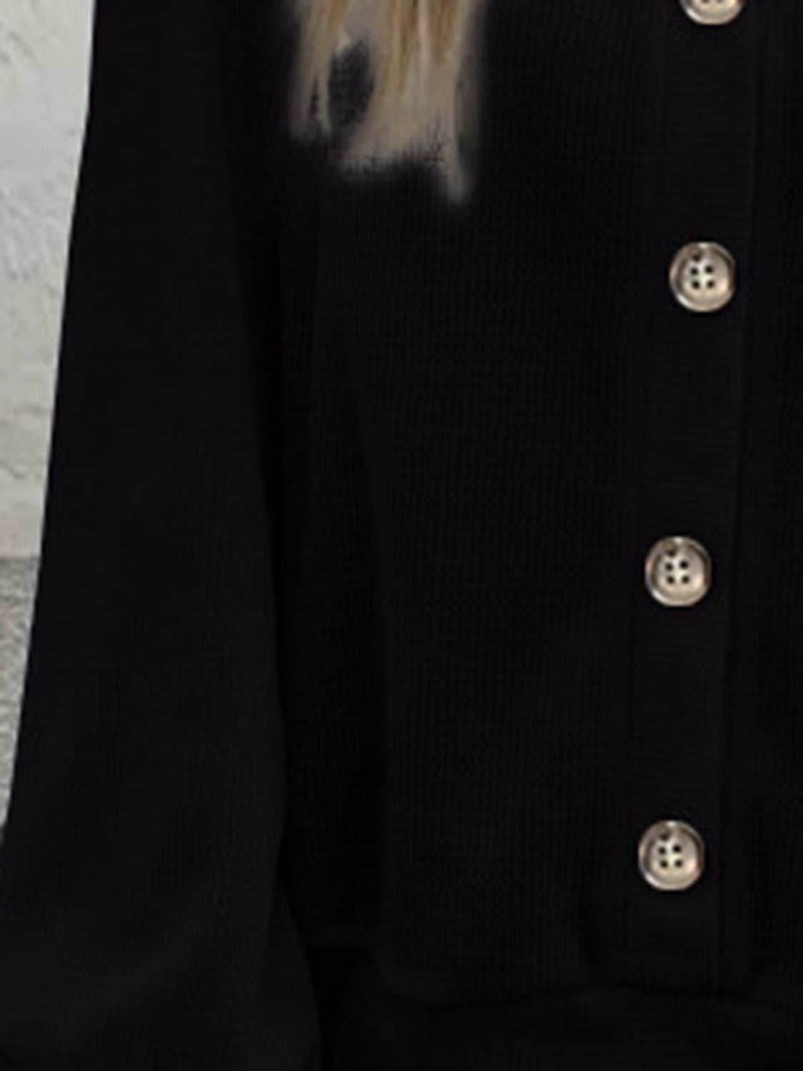 Texture detail of the black waffle-knit V-neck blouse, capturing the fabric's soft feel.