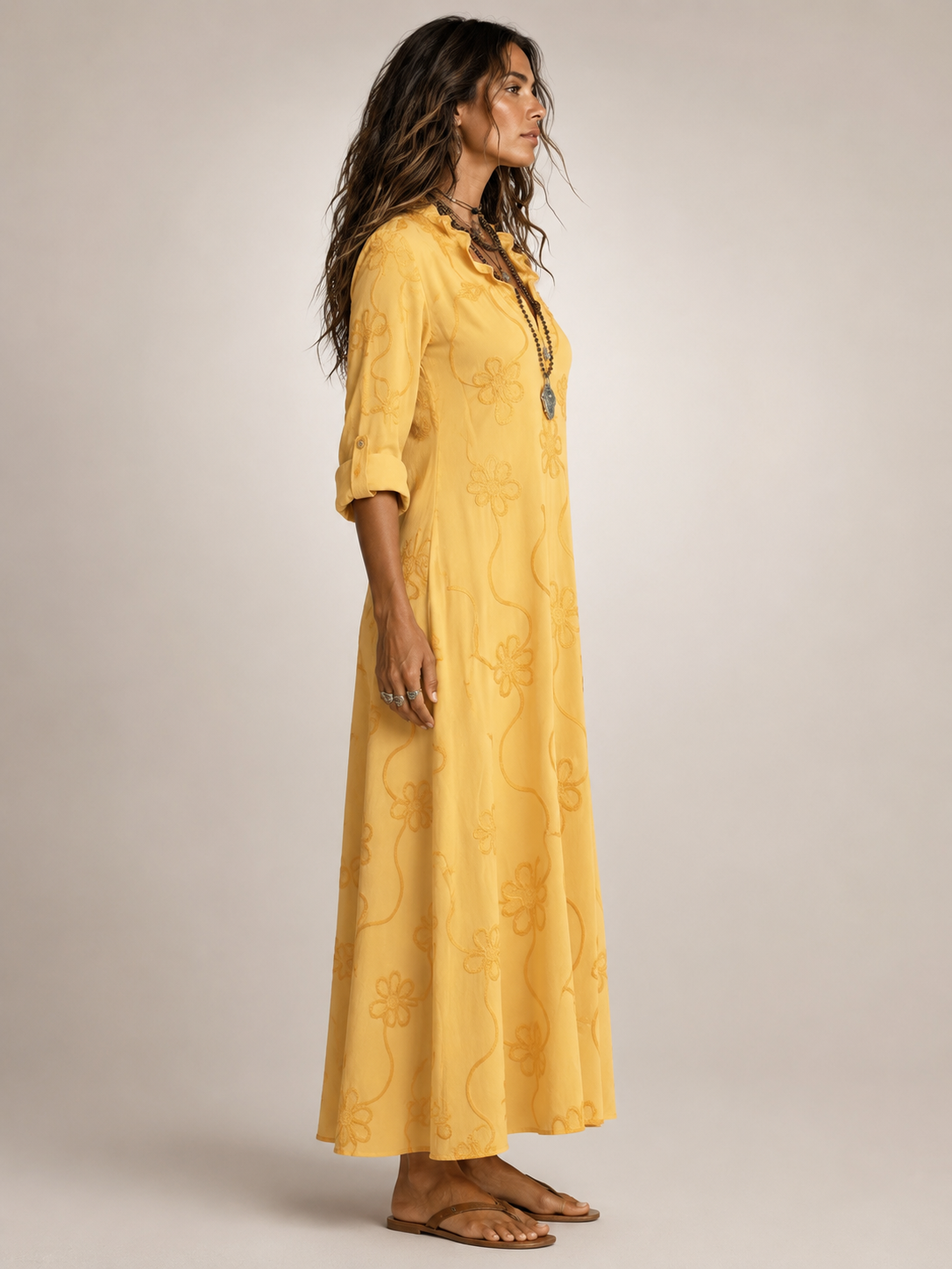 Side profile of a woman showcasing the relaxed fit of the yellow floral flowing maxi dress in a natural setting.