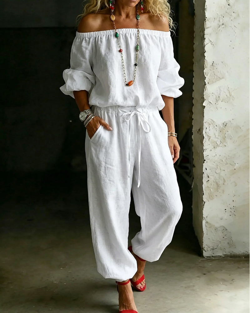 Full front view of the Rhiannon off-shoulder cotton jumpsuit in a light neutral shade, showcasing its relaxed fit and tie-waist detail.