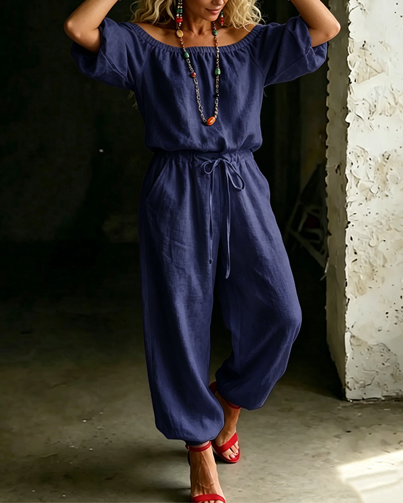 Stylised shot of the Rhiannon off-shoulder cotton jumpsuit paired with minimal accessories for a chic look.