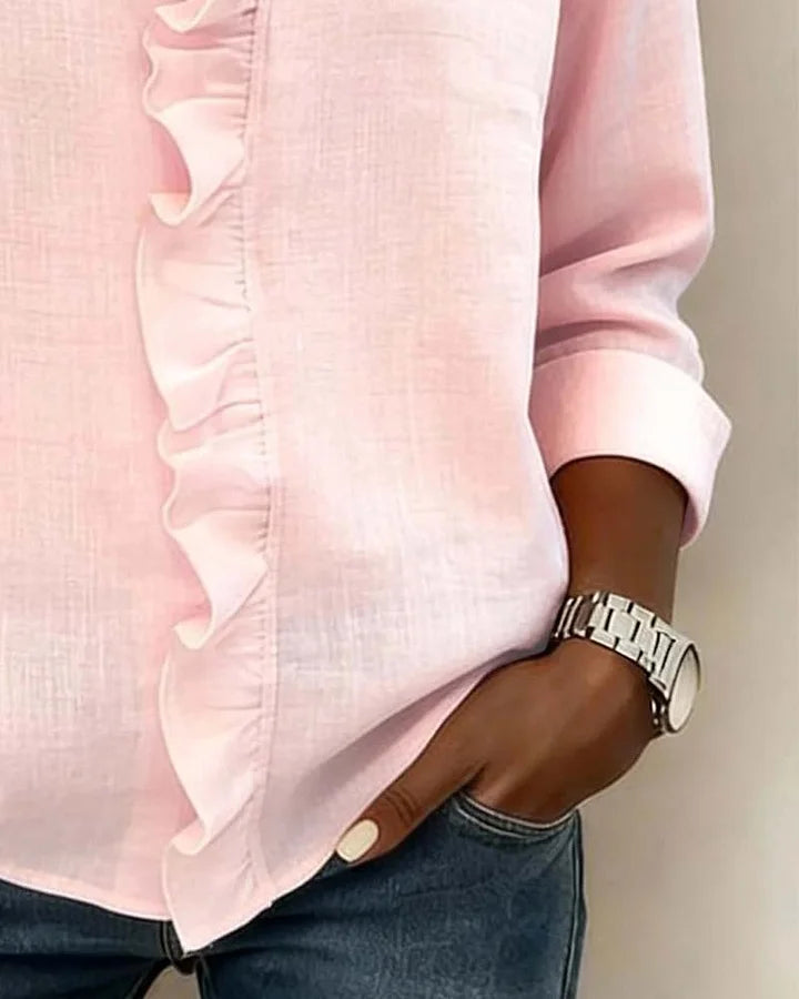 Three Persephone ruffled V-neck blouses in different colours (pink, white, black) hanging on a rail.