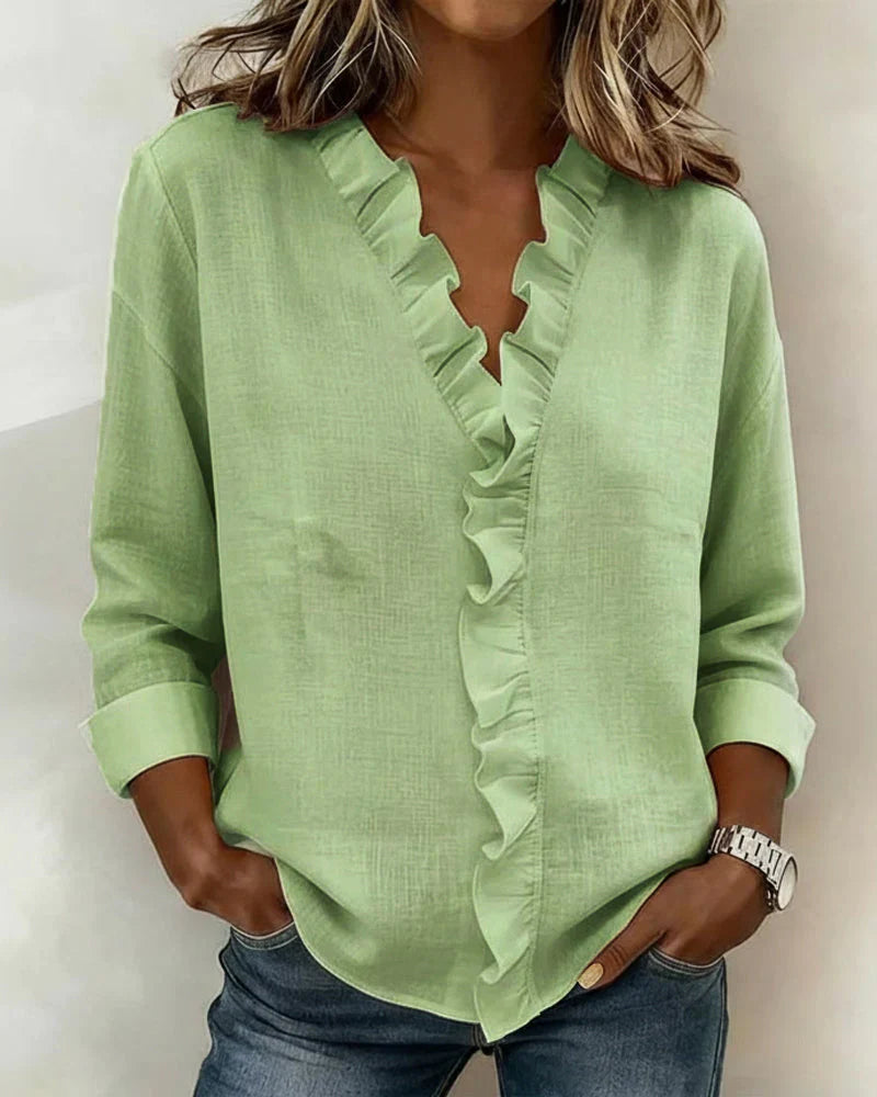 Side profile of a woman wearing the Persephone ruffled V-neck blouse in pink, styled with trousers.