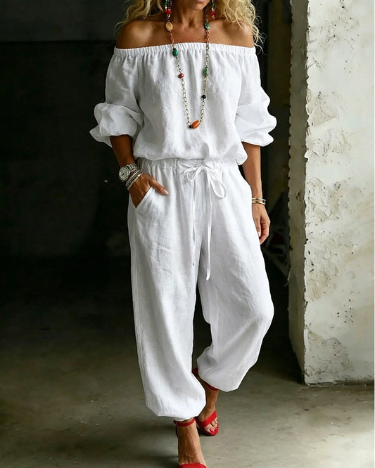Front view of a model elegantly posing in a white Seraphina cotton off-shoulder jumpsuit, showcasing its relaxed fit.