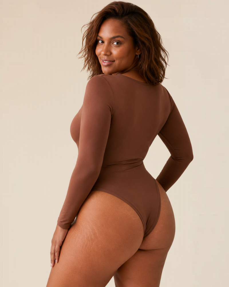 Lifestyle image of a woman wearing a black long sleeve thong bodysuit tucked into high-waisted trousers, exuding effortless style.